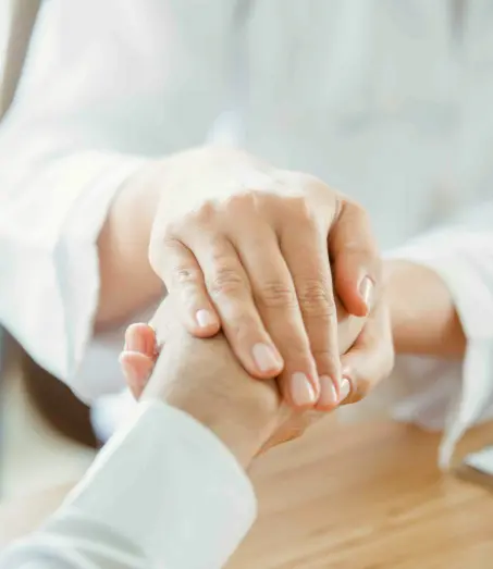 Eine Person mit einem weißen Kittel hält vertrauensvoll die Hand einer anderen Person.