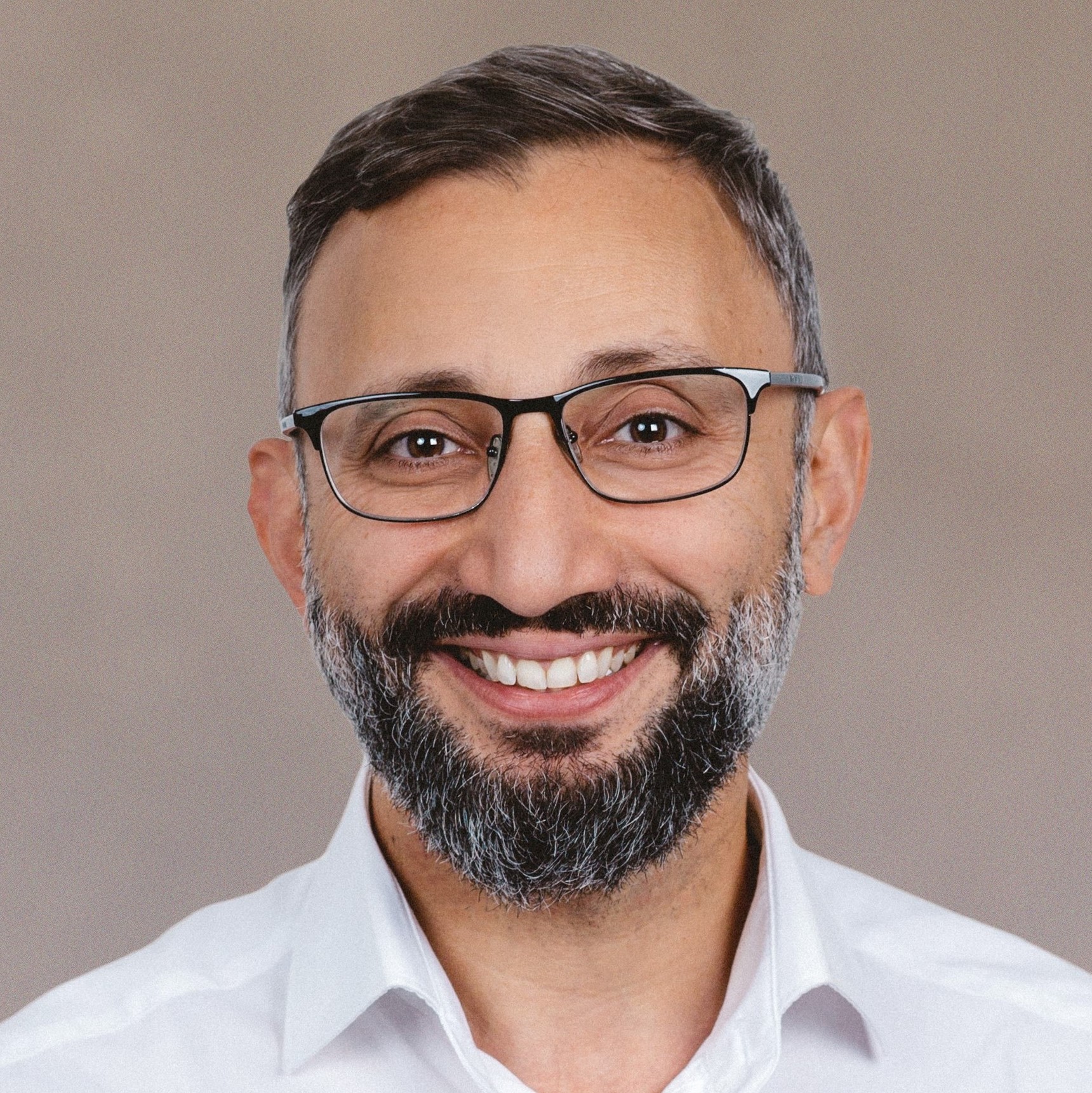 Porträtfoto von einem lächelnden Mann mittleren Alters mit Brille und kurzen Haaren vor hellgrauem Hintergrund